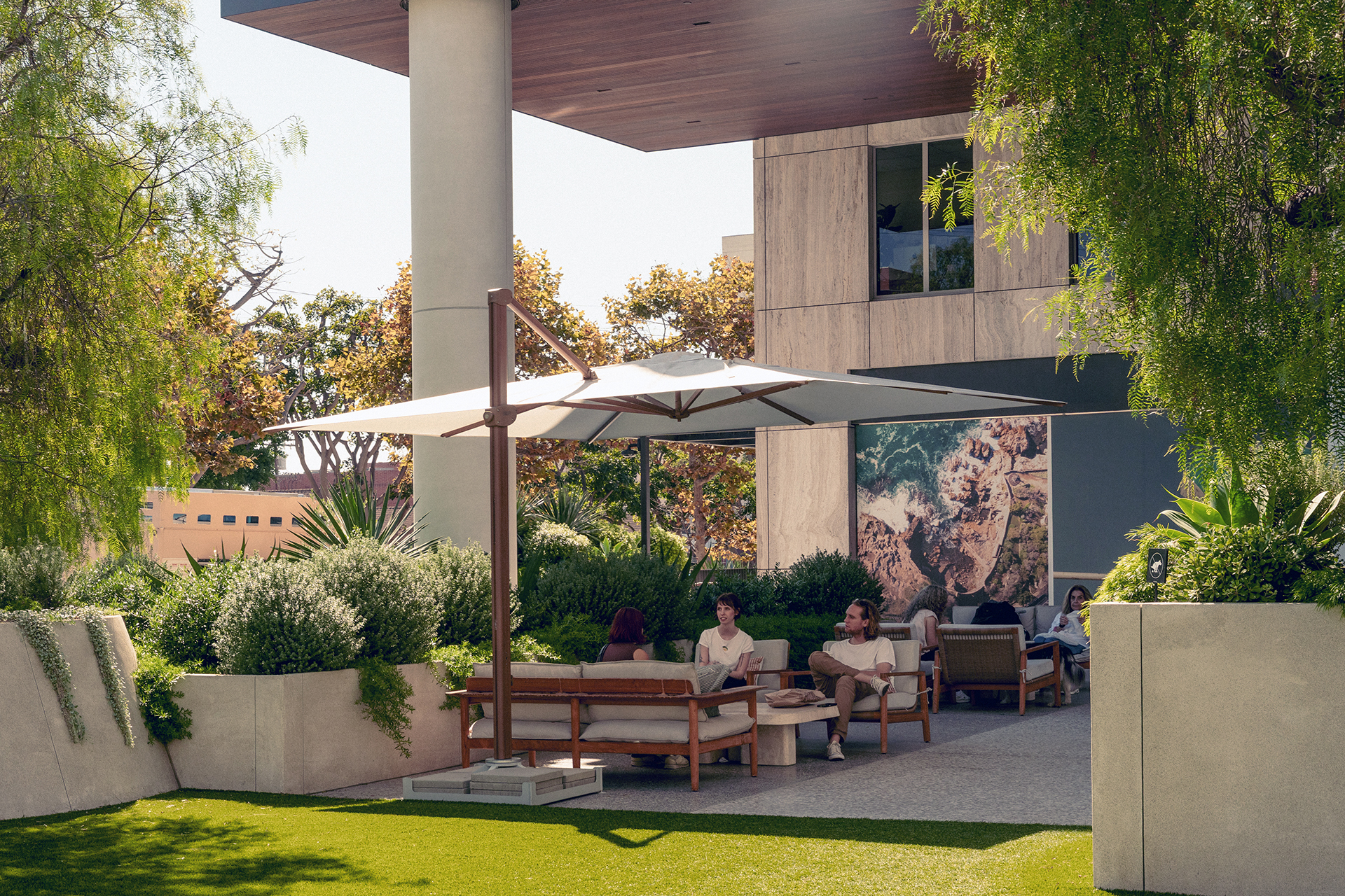 A modern outdoor space with seating under a large umbrella, surrounded by greenery and a prominent wall art installation.
