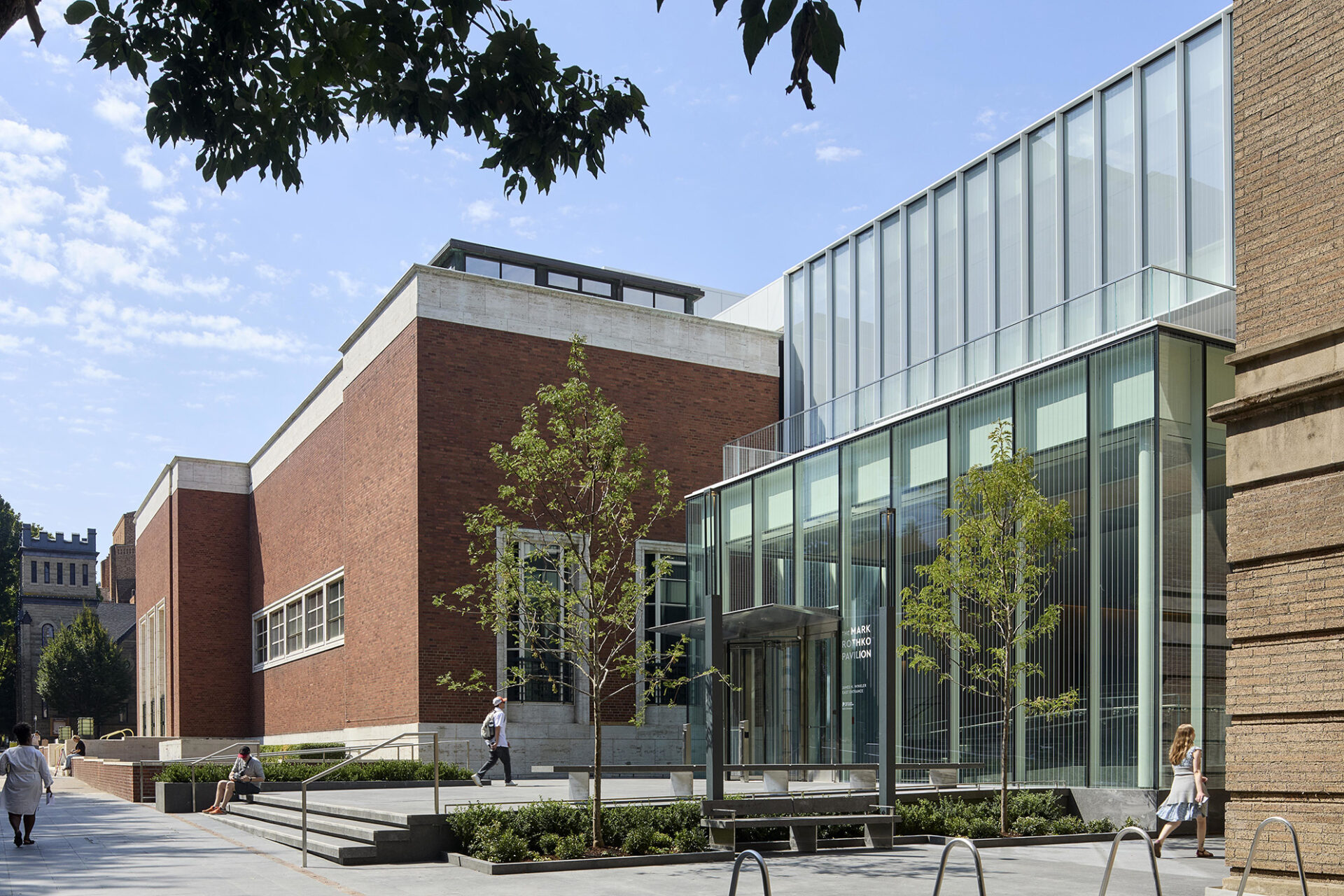 Modern architectural design featuring the Rothko Pavilion with brick and glass elements, surrounded by landscaped greenery and clear skies.